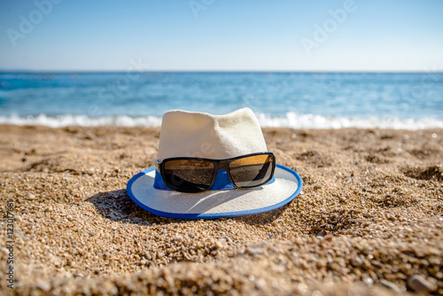 Beach hat and sunglasses lying on the sand by the sea