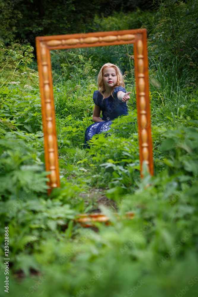 Obraz premium Portrait of beautiful little girl in the blue dress in nature with a mirror