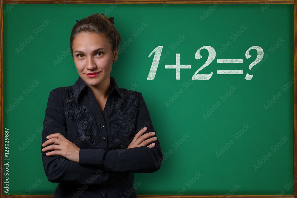 Beautiful young woman teacher (student, business woman) in classical dress standing near a blackboard with the inscription one plus one equal two Beautiful young woman teacher (student, business woman) in classical dress standing near a blackboard with the inscription one plus one equal two