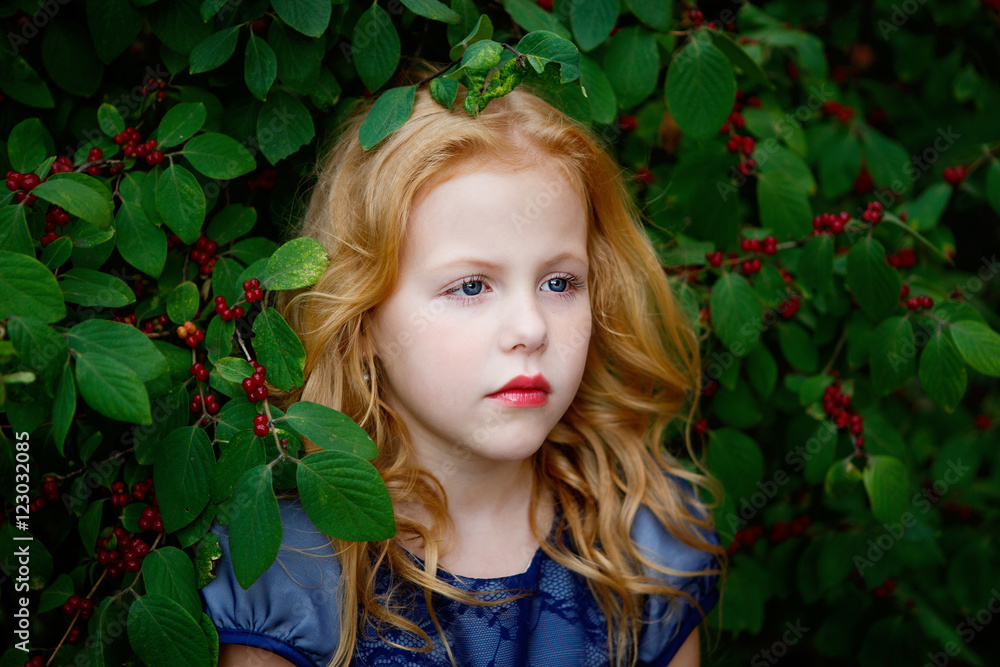 Portrait of beautiful little girl in a blue dress on a background of leaves cherries Portrait of beautiful little girl in a blue dress on a background of leaves cherries