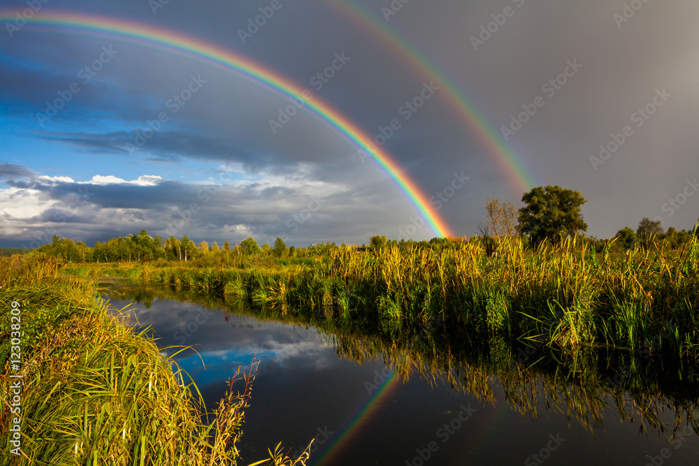 Naklejka premium Amazing double rainbow over the small rural river.
