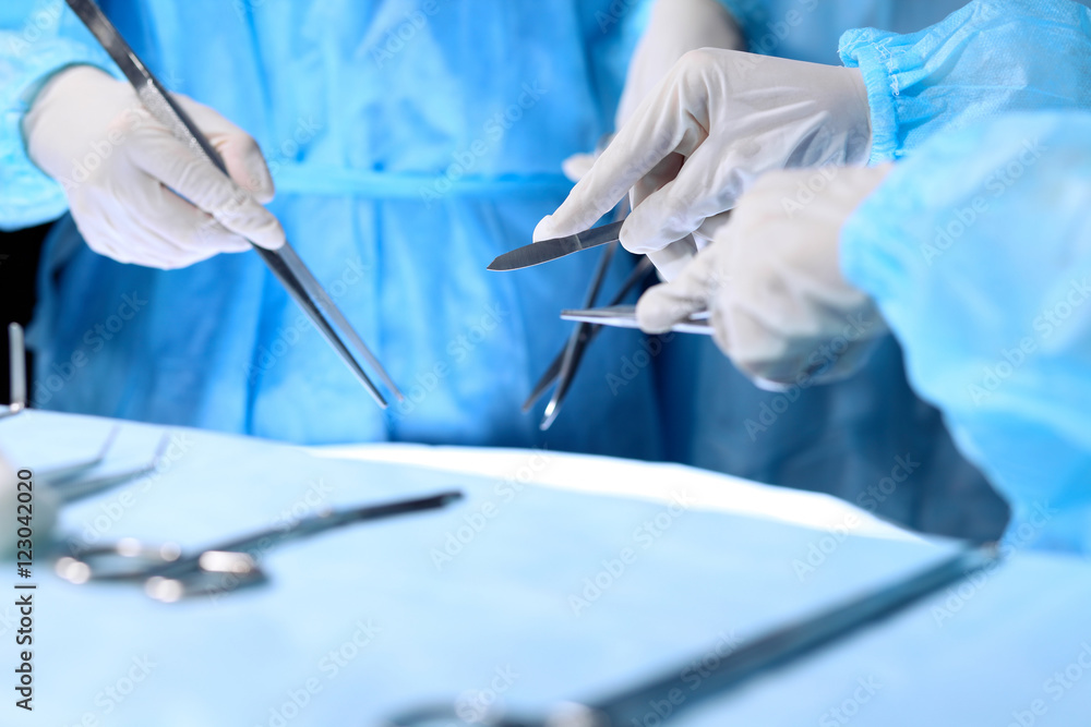 Medical team performing operation. Group of surgeon is working in operating theatre toned in blue Medical team performing operation. Group of surgeon is working in operating theatre toned in blue