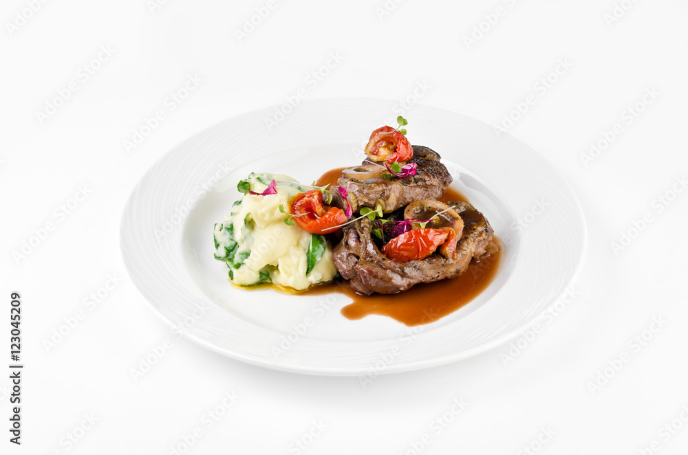 Braised beef on the bone with dried tomatoes and mashed potatoes with spinach and feta cheese on a plate on a white background