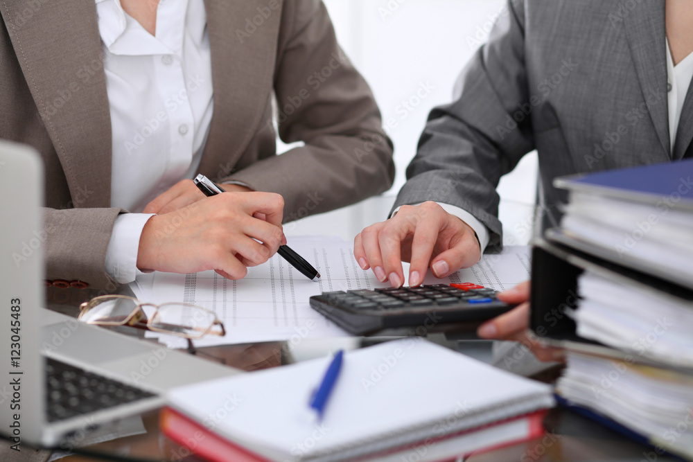 Two female accountants counting on calculator income for tax form completion hands closeup. Internal Revenue Service inspector checking financial document. Planning budget, audit concept Two female accountants counting on calculator income for tax form completion hands closeup. Internal Revenue Service inspector checking financial document. Planning budget, audit concept