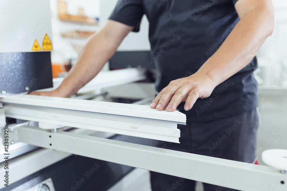 Manual worker doing his job on big machine for profile cutting. Manufacturing jobs. Selective focus. Factory for aluminum and PVC windows and doors production. Manual worker doing his job on big machine for profile cutting. Manufacturing jobs. Selective focus. Factory for aluminum and PVC windows and doors production.