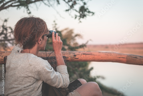 Tourist watching wildlife by binocular on Chobe River, Namibia Botswana border, Africa. Chobe National Park, famous wildlilfe reserve and upscale travel destination. Toned image. photo
