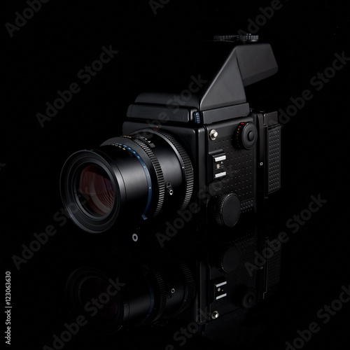 Proffessional medium format film camera with prism finder and portrait lens attached on isolated black background with reflection.