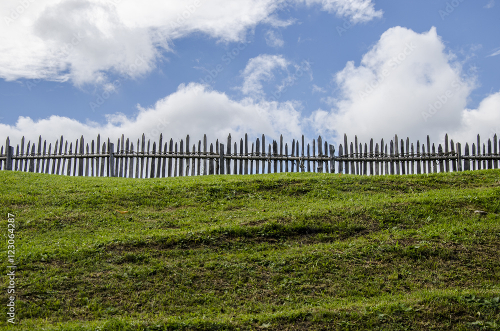 a wooden fence divide a green mountain field from the blue sky