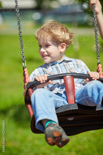 Little blond boy having fun on chain swings