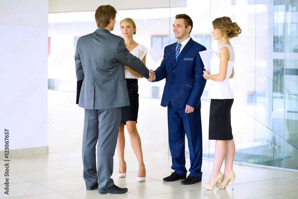 Fototapeta premium Businessmen shaking hands. Two confident businessmen shaking hands and smiling while standing at office together with people in the background