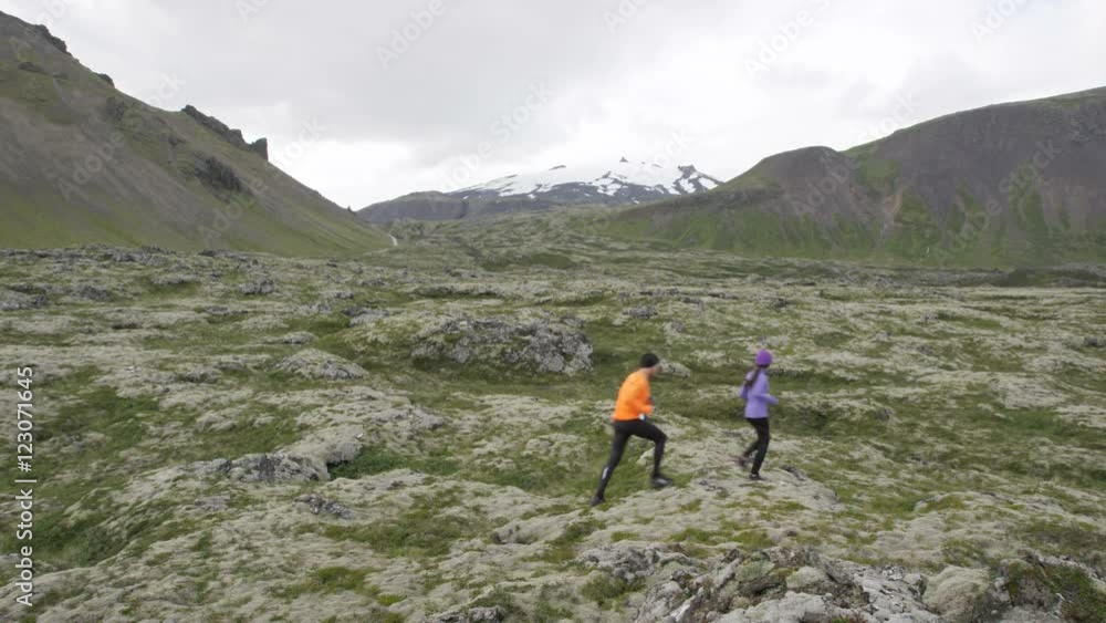 Exercise running sport. Runners on cross country trail run outdoors working out. Fit young fitness model man and asian woman training together outside in mountain nature on Snaefellsnes, Iceland.