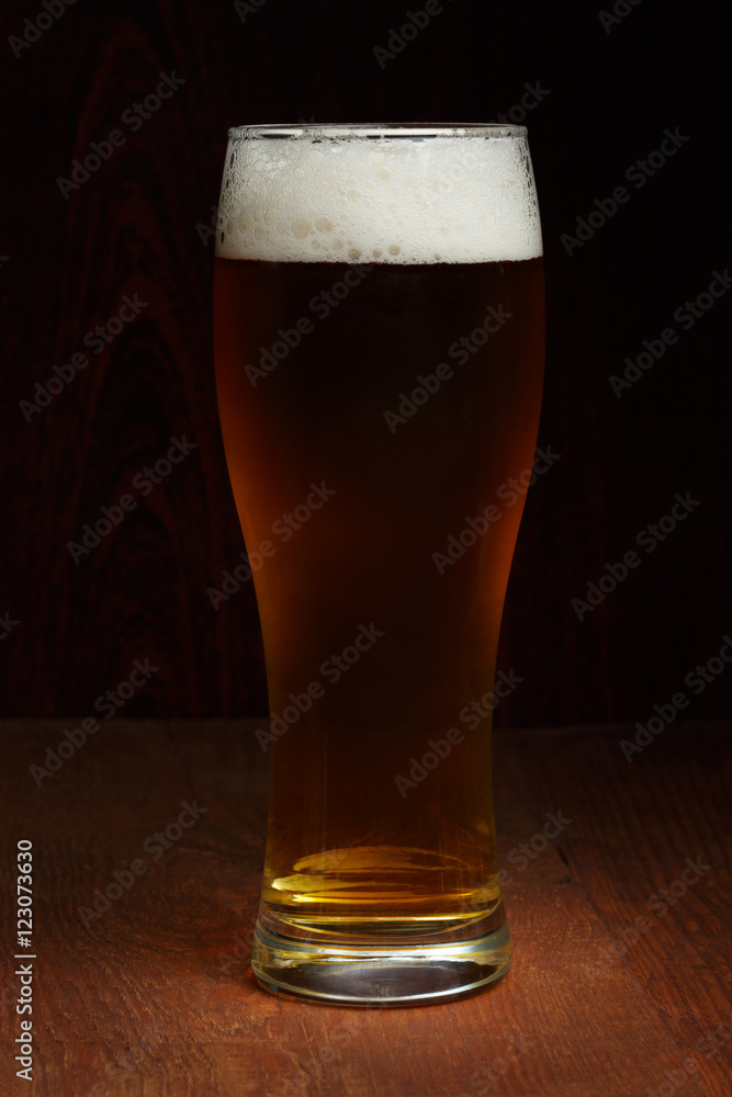 Dark beer in glass standing at wooden background