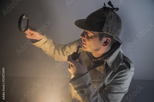 sherlock holmes in studio etective at work with magnifying glass and pipe
