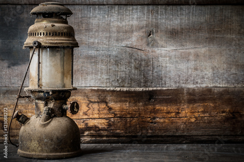 Old fashioned vintage kerosene oil lantern lamp burning with a soft glow light with aged wooden floor with copy space