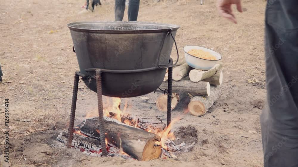 Cooking soup with lamb in a cauldron on a wood stove in the autumn. A man is mixing braised lamb, onion and bell pepper in the cauldron. Cooking soup with lamb in a cauldron on a wood stove in the autumn. A man is mixing braised lamb, onion and bell pepper in the cauldron.
