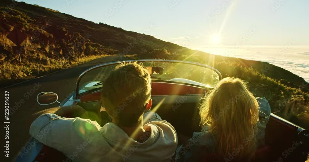 Happy couple driving on country road into the sunset in classic vintage sports car