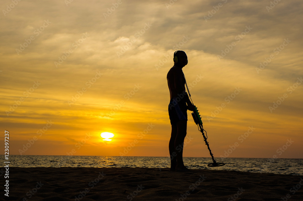 Treasure hunter with Metal detector on sunset  the beach