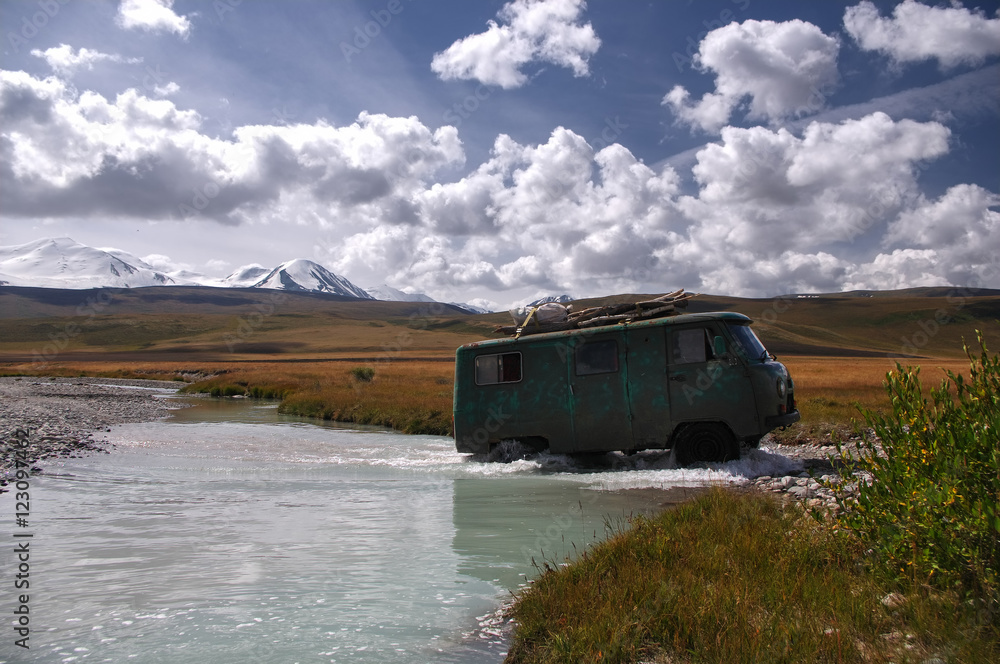 Off-road car moving mountain river at a ford on the background of snowy peaks, Plateau Ukok, Altai mountains, Siberia, Russia