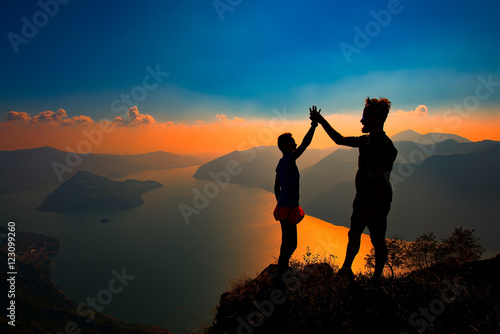 A pair shake hands in victory on top of a mountain