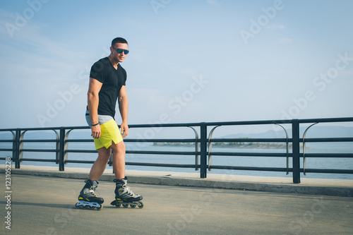 young man with inline skates ride in summer park seafront outdoor rollerskater