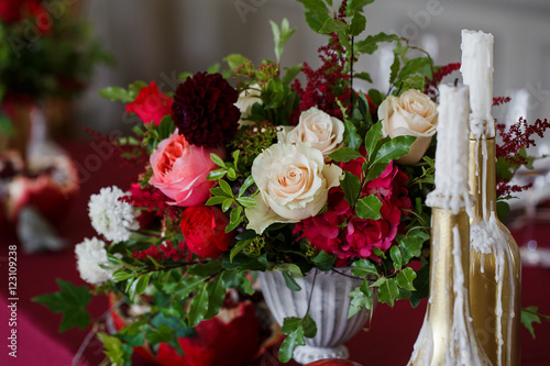 Rich red bouquet in Greek vase stand behind golden bottles with