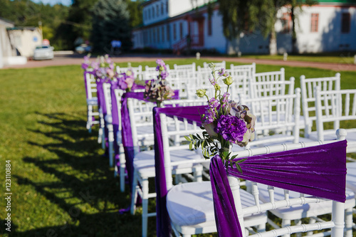 White chairs deocrated with violet cloth and flowers stnad in ra photo