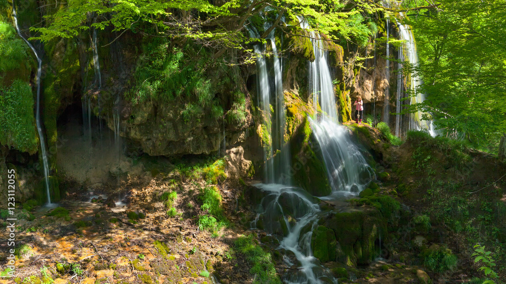 Obraz premium Woman standing next to a waterfall at the idyllic day
