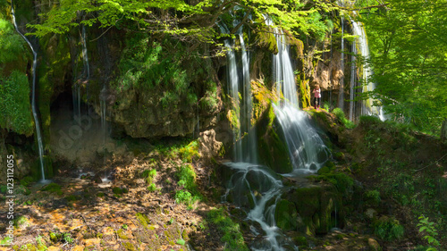 Woman standing next to a waterfall at the idyllic day