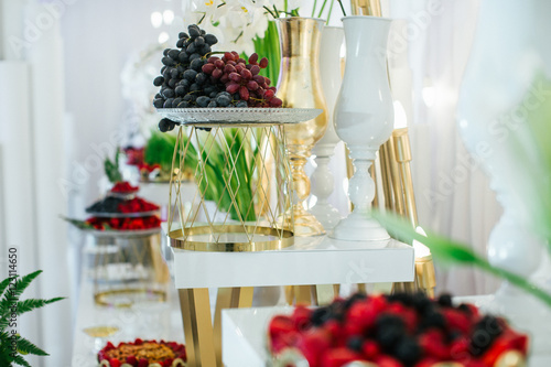 Berries and fruits lie on steel plates on the white buffet