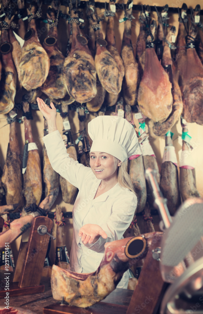 Woman wearing uniform showing  ham in meat shop