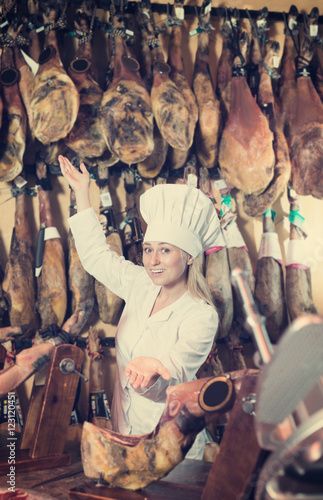 Woman wearing uniform showing ham in meat shop