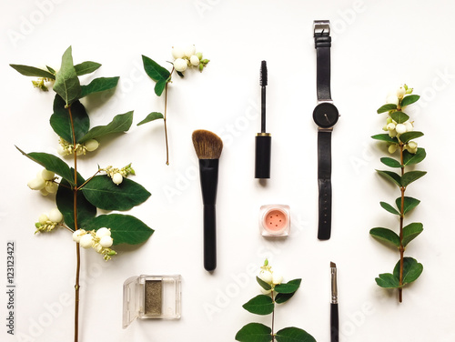 Colorful composition with woman make up tools and accessories, decorated with green snowberry branches. Flat lay on white table, top view