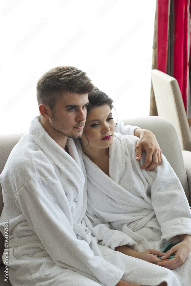 Happy young couple sitting on couch in bathrobe Happy young couple sitting on couch in bathrobe