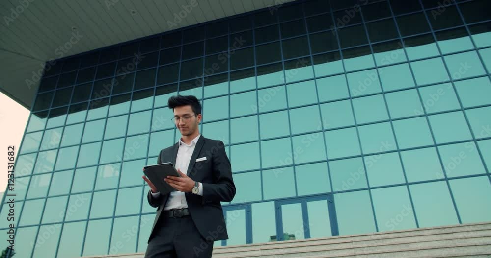 young ethnic businessman working with the tablet, goes on the steps in front of the business building, slow motion young ethnic businessman working with the tablet, goes on the steps in front of the business building, slow motion
