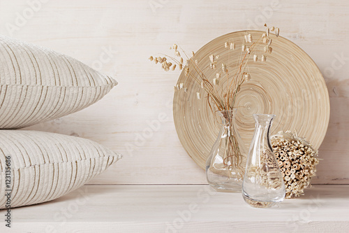 Soft home decor of  glass vase with spikelets and pillows on white wood background. Interior.