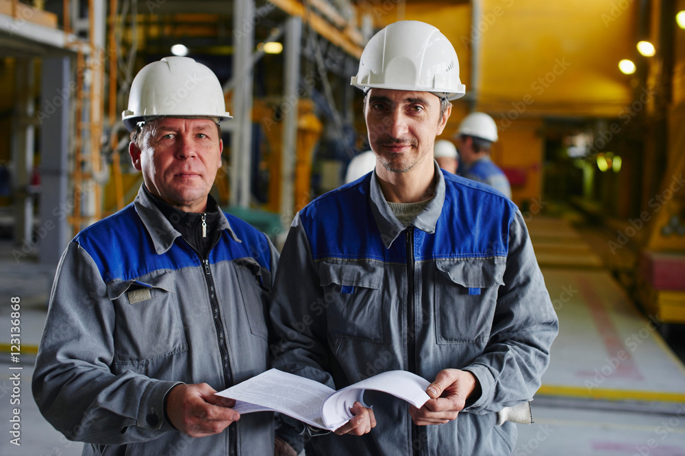 A man in overalls and a helmet stands near a kiln and holding a brick A man in overalls and a helmet stands near a kiln and holding a brick