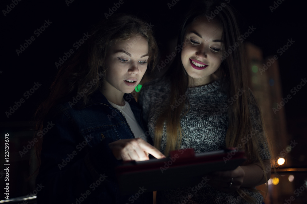 Two women look down to digital tablet in balcony at night Two women look down to digital tablet in balcony at night