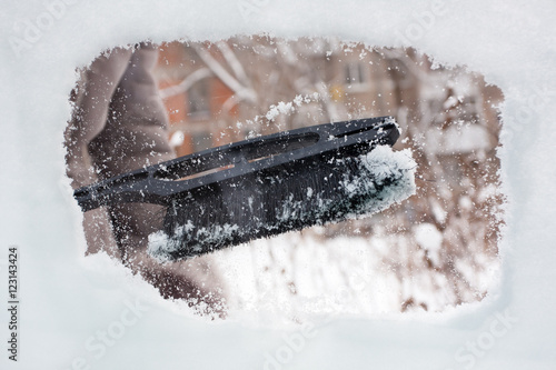 hand cleaning snow-covered window of car with brush