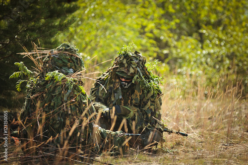 two men in camouflage sitting in the grass