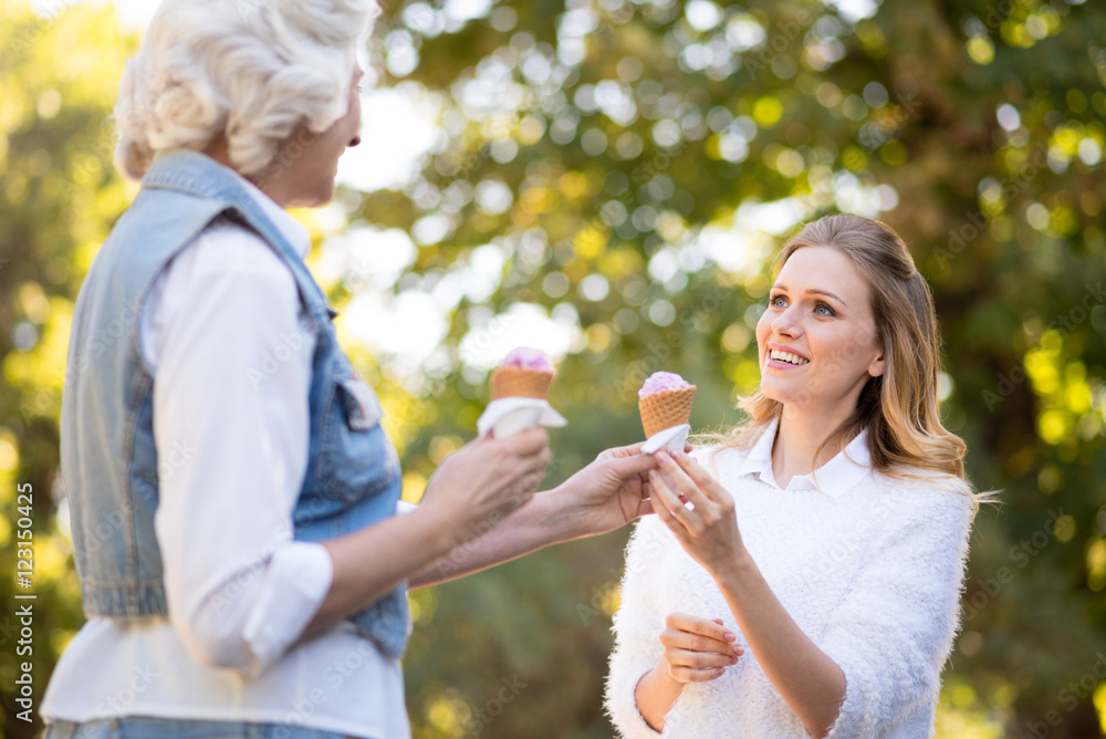 Obraz premium Gray haired pretty woman giving an ice cream to her daughter.