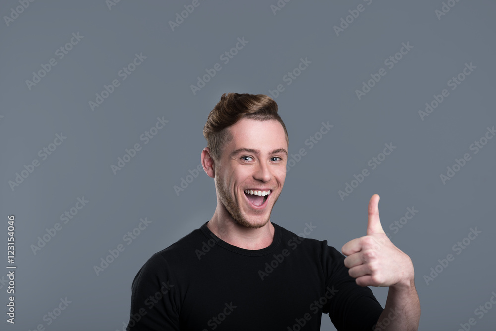 Cheerful young man smiling and raising thumb Cheerful young man smiling and raising thumb