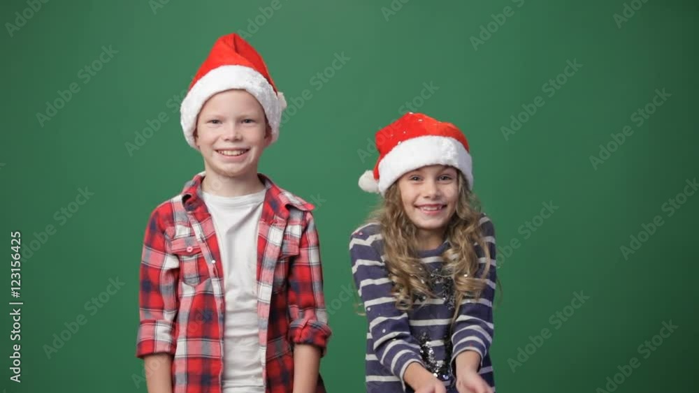 Couple of children in christmas caps throwing up confetti, green screen background Couple of children in christmas caps throwing up confetti, green screen background