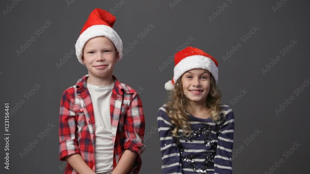 Couple of children in christmas caps throwing up confetti, gray background Couple of children in christmas caps throwing up confetti, gray background