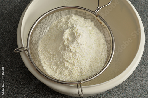 Sifting flour into a white plastic bowl