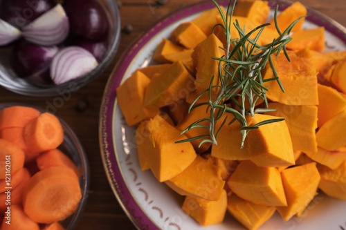 Food ingredients for cooking of traditional creamy pumpkin soup consist from chopped hokkaido pumpkin with fresh green rosemary sticks, red onion chopped in quaters and red carrot chopped to rings. photo