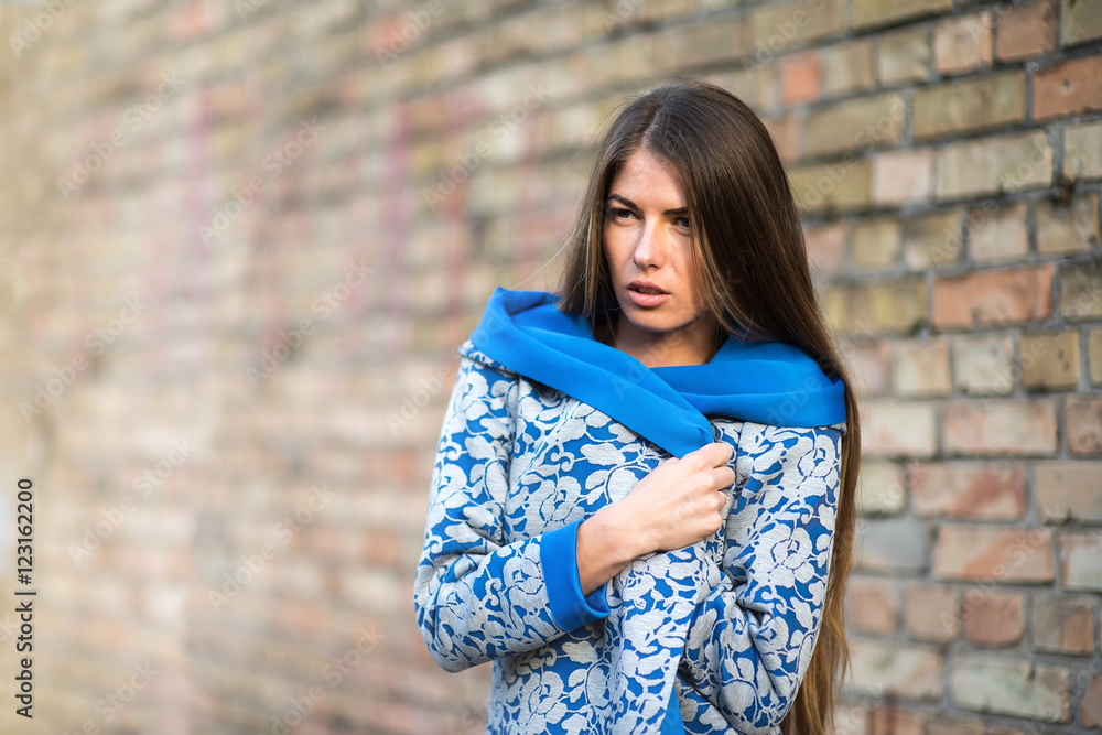 Young woman wrapped in a coat at the wall . Girl thoughtfully looks past the camera. Young woman wrapped in a coat at the wall . Girl thoughtfully looks past the camera.