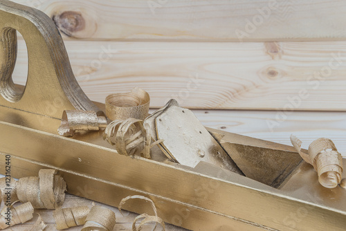 Golden jack-plane with golden shavings on a wooden background photo