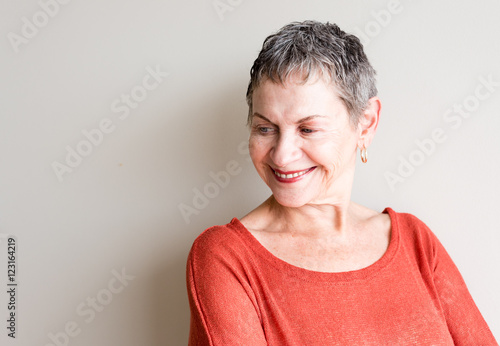 Older woman with short grey hair and orange top smiling