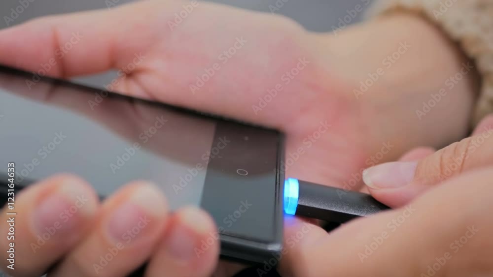Woman's hand plugging black lightning charging cable into smartphone - USB data cable connecting on modern gadget. Close up shot Woman's hand plugging black lightning charging cable into smartphone - USB data cable connecting on modern gadget. Close up shot