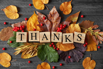 Autumn composition of leaves, berries and cubes with word THANKS on wooden background. Thanksgiving day concept